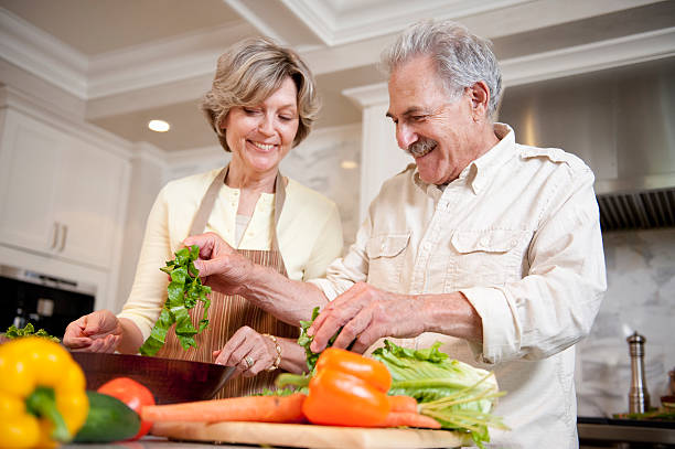 Couple de retraités en train de cuisiner une salade de légumes froids