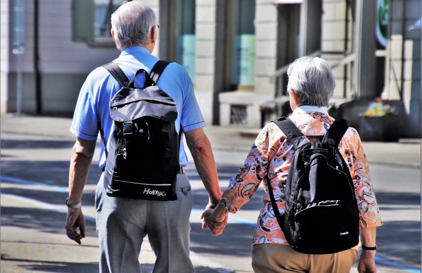 deux personnes agées de dos avec des sacs à dos se tenant la main