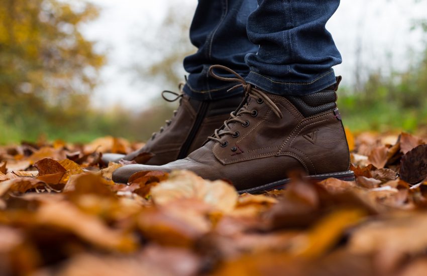 zoom sur les pieds d'un homme portant des bottines marron sur sol recouvert de feuilles mortes